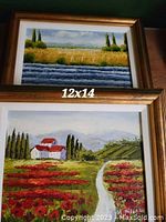 Both framed oil paintings showing landscape scenes: one wheat field with river, one rural path with flowers and house. Each 12x14 inches with gold frames and white mats.