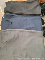 Four pairs of Perry Ellis men's dress pants laid flat showing colors and designs: dark grey, navy blue, light grey, and black.