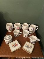 Overview of four large mugs, three small mugs, creamer pitcher, sugar bowl with lid and coasters on table