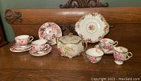 Full view of entire set on wood surface, showing all cups, saucers, plates, and lidded dish with rose decorations