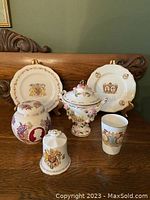Group photo showing all six items; two plates in the back on stands, the covered urn in center front, bell and small jar in front, and commemorative glass on right