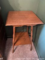 Side view of antique square parlour table showing turned legs and lower shelf.