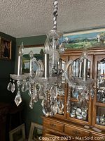 Full view of clear crystal chandelier with four arms and hanging crystal pendants, shown lit by ambient room light.