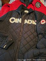Close-up of black jacket with 'CANADA' print and maple leaf patch on sleeve, showing quilting and collar details.