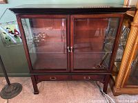 Full front view of dark wood display cabinet with two glass doors and two small drawers at the base.