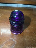 Front and top view of antique glass insulator showing deep amethyst color and surface wear.