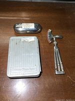 Top-down view showing all three items on a wooden surface: metal syringe kit case, white plastic medical emergency kit, and reflex hammer with multiple attachments folded in handle