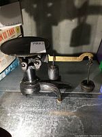 Side view of antique black cast iron scale with a round weighing platform, brass weighing arm, sliding weight, and hanging weight.