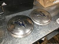 Pair of 1930s Ford V8 7 inch diameter metal hubcaps on metal surface showing front with V8 emblem