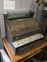 Front view showing ornate brass façade, key buttons, marble shelf and open cash drawer
