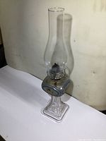 Full view of the lamp showing the tall clear glass chimney and ornate base with floral design