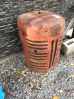 Front and side view of antique tractor front end grille, showing round top, horizontal slats and rusted red paint.