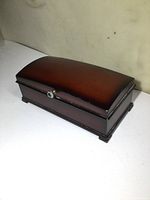 Wooden Bombay musical jewelry box with domed hinged lid and front metal knob, polished wood finish.