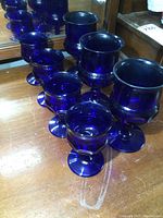 Seven cobalt blue glass goblets arranged in two rows showing both small and large sizes.