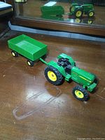 Full view of ERTL John Deere tractor hooked to wagon on wooden surface with mirror behind.