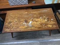 Top view of rectangular rosewood coffee table showing extensive inlay of rural life scenes including people, huts, trees, animals, and birds
