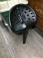 Black cast iron Massey Harris tractor seat photographed from side angle showing shape and mounting bracket.
