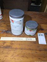 Two unopened Country Chic paint jars and a wooden stir stick on a wooden surface.