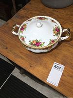 Royal Albert Old Country Roses 1962 covered serving dish with handles, displayed on wooden table, showing top, side, and angled views. Gold trim and floral rose pattern visible.