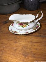 Side angled view of the Royal Albert Old Country Roses gravy boat on its attached plate showing handle and floral pattern.