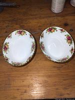 Two oval serving bowls with floral pattern and gold rim on wooden table