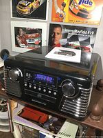 Front and slightly side angle view of the black stereo system with visible control panel, display screen, and speaker grills.