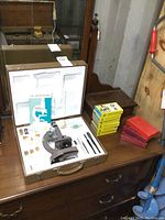 Overview of the microscope kit inside an open carrying case on a wooden dresser including microscope, accessories, and external boxes of slides.