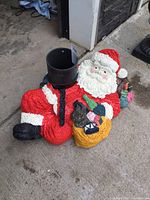 Full side angle view of vintage Santa Claus Christmas tree holder showing Santa reclining and holding a yellow bag of presents and green bottle, with black boots and red suit.