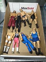 Top view of all 8 wrestling action figures laid flat inside cardboard box. Various colorful wrestling outfits visible.