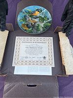 Photo showing the painted Baltimore Oriole plate along with the certificate of authenticity inside protective packaging.