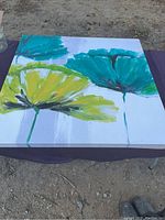 Flower painting print laid flat on outdoor surface showing teal and yellow-green flowers.