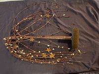 Photo of decorative mini tree lying on a dark fabric background showcasing thin metal branches with star and berry ornaments and a round weighted metal base.