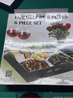 Box with image and text indicating a 6-piece gourmet cheese serving set by Roscher & Co., showing the set filled with olives, nuts, cheeses, and crackers.