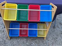 Front view showing all 8 multicolored bins in a wooden frame on a dirt ground.
