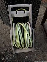 Garden hose coiled on beige plastic spinning reel cart with handle, set on dirt ground outdoors.