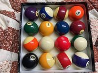 Top-down view of the 16 pool balls in the box showing number and colors.