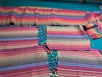 Photo displaying 3 of the woven textile items including 2 table mats and 1 table runner with colorful striped pattern and fringed edges.