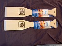 Two wooden BBQ scrapers placed flat showing front with branding and product label detailing they are a wooden BBQ scraper from iHome made in Canada, new condition.