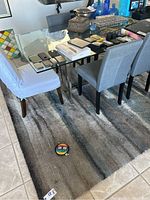 Large floor rug under dining table with chairs, showing striped pattern in neutral shades of gray and beige.