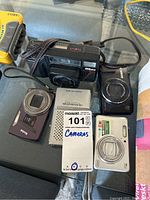 Wide view of all cameras and the weather radio on a glass table with a MaxSold lot tag.