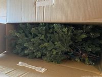 Boxed artificial Christmas tree showing folded branches in cardboard box.