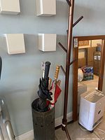 Full view of wooden coat rack with metal umbrella stand holding five umbrellas of various types and colors.