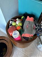 Wooden bowl filled with various dog toys, tennis balls, and a dog sweater visible on top.
