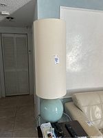 Side view of a single lamp showing light blue glossy ceramic globe base with tall cylindrical beige fabric shade