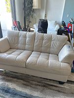 Front and side view of the light beige leather love seat sofa showing tufted cushions and minor wear on right armrest.