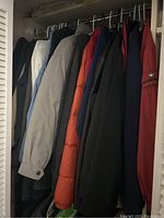 Photo showing a variety of men's jackets hanging on rack, including casual coats and puffer jacket in grey, blue, light gray, orange, and black.