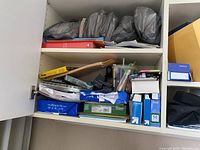Closed cabinet door showing items such as multiple envelopes, boxes, and plastic containers with pens.