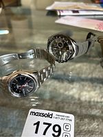 Two Seiko watches displayed on glass surface with lot tag 179