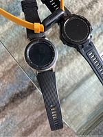 Four smart watches on glass table, varied styles and straps visible