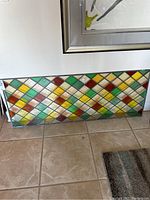 Full view of the colorful stained glass panel laid on the floor showing diamond pattern and metallic frame.